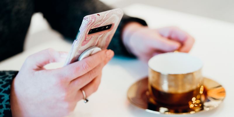 Kvinne med mobil og kaffekopp, illustrasjonsfoto